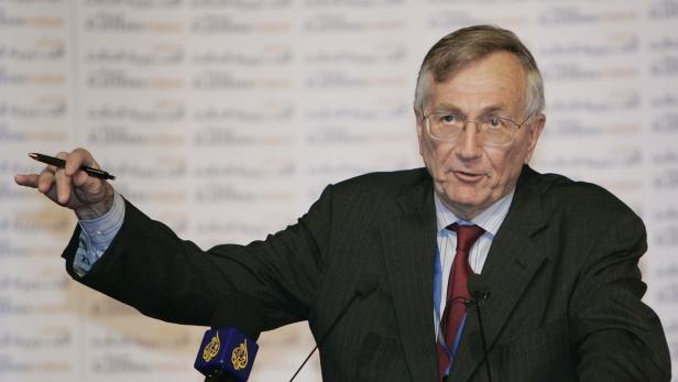 Ein Mann mit Brille und Anzug gestikuliert mit einem Stift in der Hand.