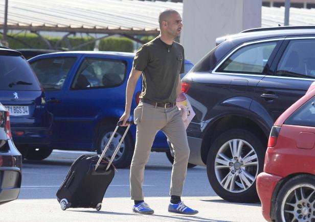 Pep Guardiola zieht einen Rollkoffer auf einem Parkplatz.