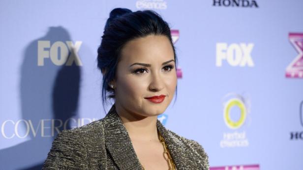Demi Lovato posiert auf einem Event vor einer Wand mit Logos.