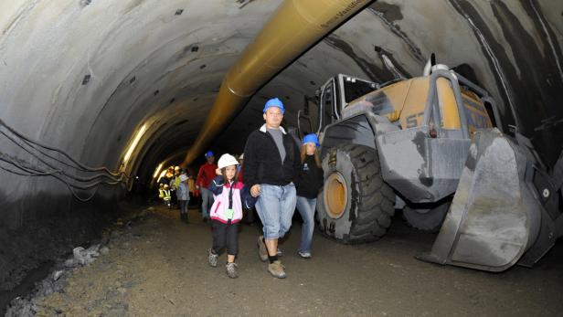 Eine Gruppe von Personen geht in einem Tunnel an einem Bagger vorbei.
