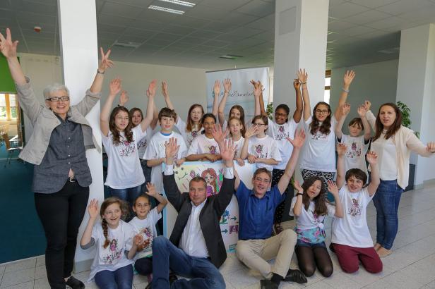 Eine Gruppe von Kindern und Erwachsenen posiert mit erhobenen Händen für ein Foto.