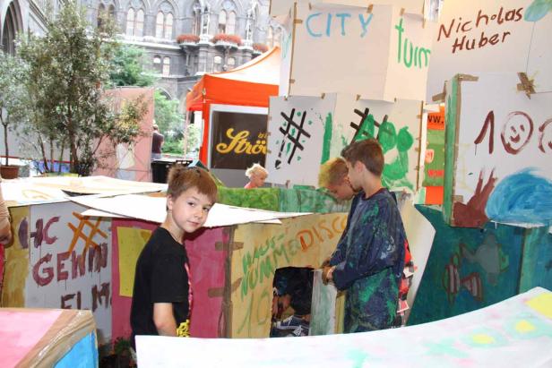Kinder spielen in einer selbstgebauten Stadt aus Kartons mit dem Schriftzug „City“.