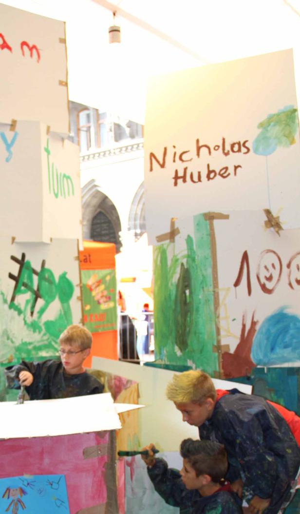 Drei Kinder bemalen Pappwände mit bunten Farben.