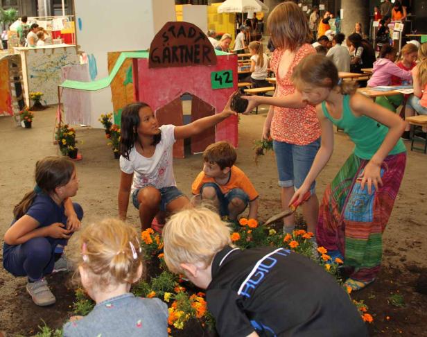 Eine Gruppe Kinder pflanzt orangefarbene Blumen in einem Beet.