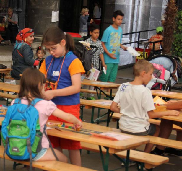 Kinder sitzen an Holztischen und beschäftigen sich mit verschiedenen Aktivitäten.