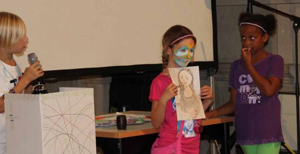 Drei Mädchen präsentieren auf einer Bühne ihre Kunstwerke.