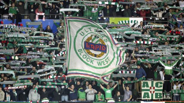 Fußballfans von Rapid Wien schwenken Schals und eine große Vereinsfahne im Stadion.
