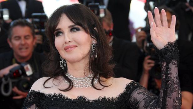 Isabelle Adjani auf dem roten Teppich mit schwarzem Kleid und erhobener Hand.