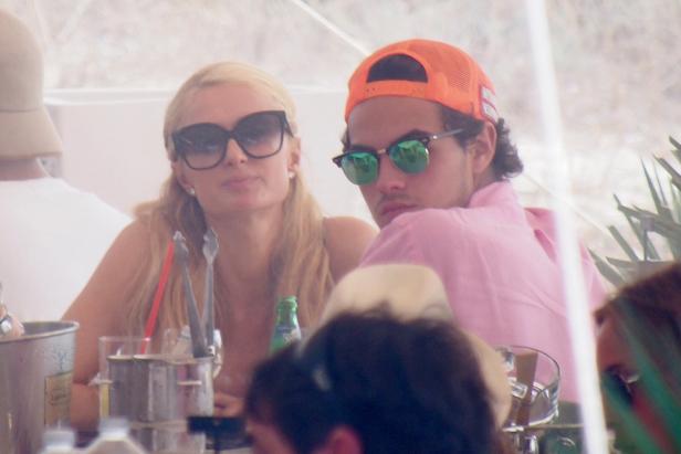 Paris Hilton und ein Mann mit orangefarbener Kappe sitzen an einem Tisch.