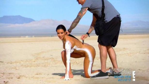 Kim Kardashian wird am Strand mit Sonnencreme bemalt.