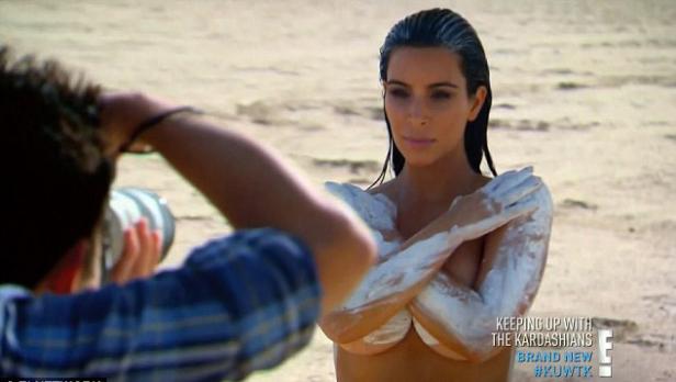 Kim Kardashian posiert am Strand mit weißer Farbe auf ihrem Körper.