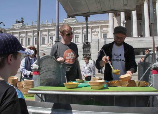 Ein Mann mit Brille serviert Essen an einem Stand vor dem Wiener Parlament.