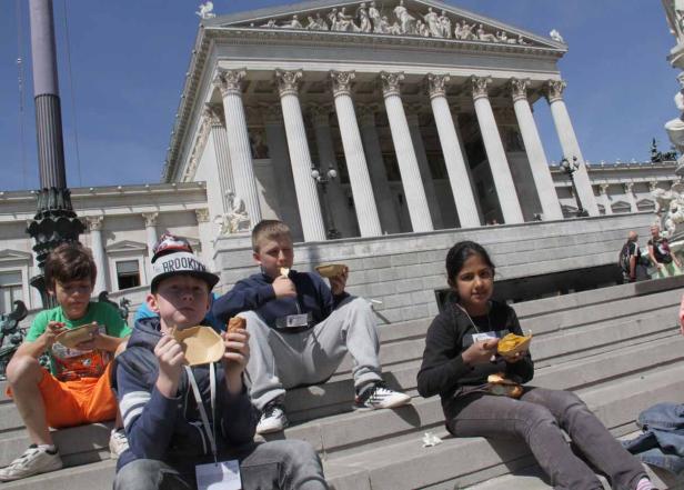 Eine Gruppe von Kindern sitzt auf den Stufen vor einem Gebäude und isst zu Mittag.