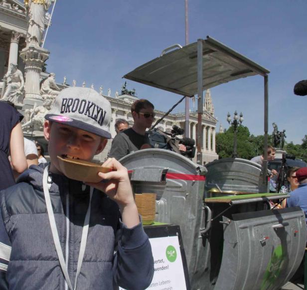 Ein Junge isst von einem Stand, der aus Mülltonnen gebaut ist, vor dem Wiener Parlament.
