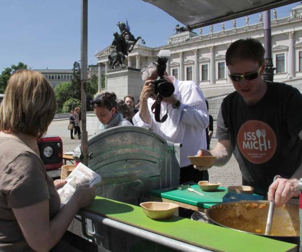Ein Mann serviert Essen von einem Stand, während ein anderer ein Foto macht.