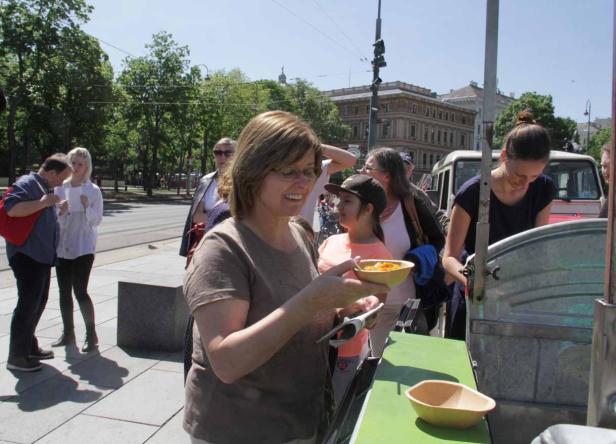 Eine Frau hält eine Schale mit Essen an einem Imbissstand im Freien.