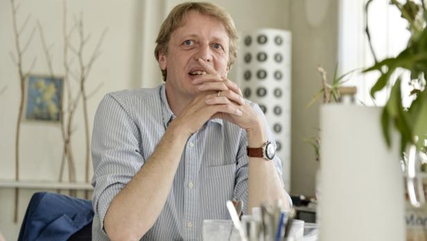 Ein Mann mit blonden Haaren sitzt an einem Tisch und spricht.
