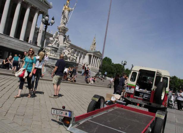 Das österreichische Parlament in Wien mit Menschen und einem Anhänger im Vordergrund.