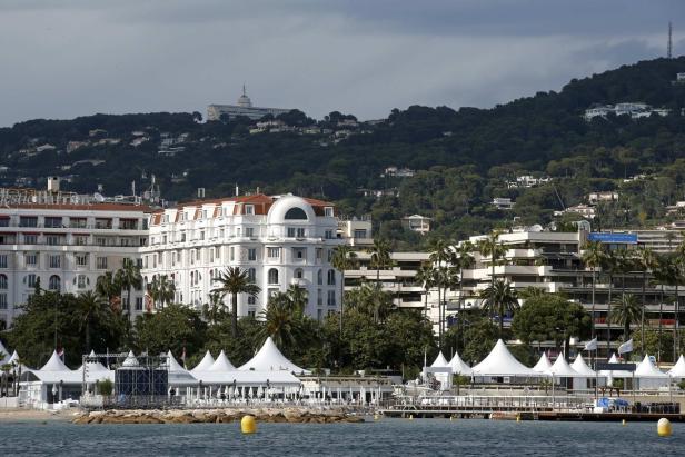 Blick auf Cannes mit weißen Zelten am Strand und einem bewaldeten Hügel im Hintergrund.