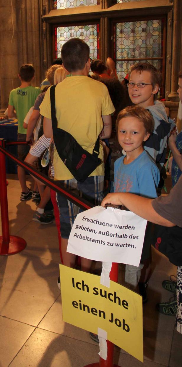 Kinder stehen in einer Warteschlange mit Schildern, auf denen „Ich suche einen Job“ steht.