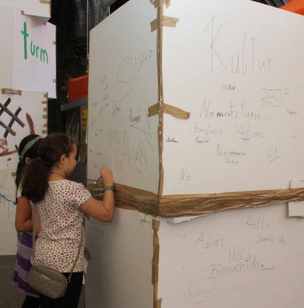 Ein Mädchen schreibt auf eine Wand, die mit internationalen Grüßen beschriftet ist.