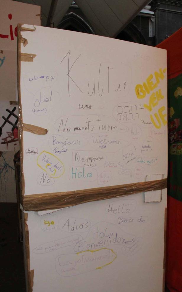 Eine mit Klebeband befestigte Tafel mit dem Wort „Kultur“ und Willkommensgrüßen in verschiedenen Sprachen.
