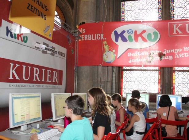 Kinder sitzen an Computern unter Bannern des „Kurier“ und „Kiku“.