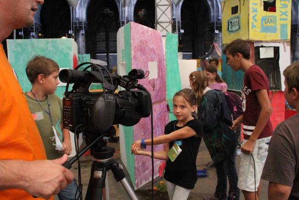 Kinder drehen einen Film mit einer professionellen Videokamera vor einer Kulisse.