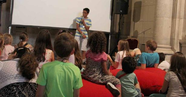 Ein Junge spricht vor einer Gruppe von Kindern in ein Mikrofon.