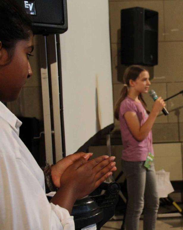 Ein Mädchen spricht in ein Mikrofon, während eine andere Person applaudiert.