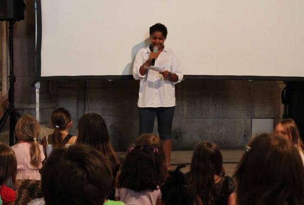 Eine Frau spricht vor einer Gruppe von Kindern in ein Mikrofon.