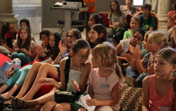 Eine Gruppe Kinder sitzt auf dem Boden und schaut aufmerksam zu.