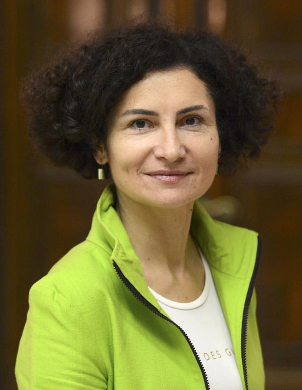 Eine Frau mit lockigem Haar lächelt in einem hellgrünen Blazer.