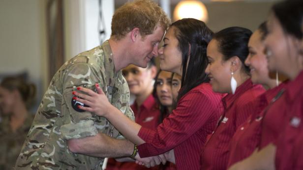 Prinz Harry berührt mit einer jungen Frau die Stirn, umgeben von weiteren Frauen in roten Hemden.