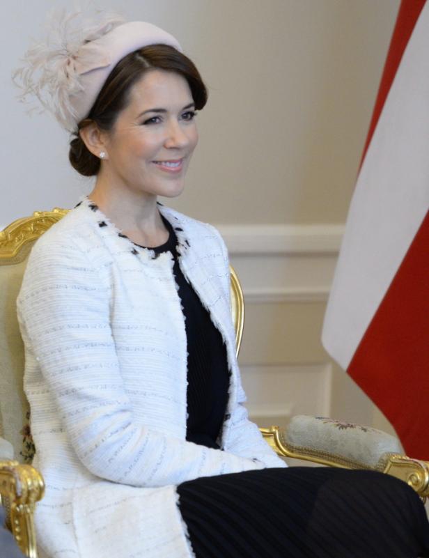 Kronprinzessin Mary von Dänemark sitzt auf einem goldenen Stuhl vor einer dänischen Flagge.