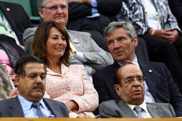 Zuschauer, darunter eine Frau in einem rosa Tweed-Jackett, sitzen bei einer Veranstaltung.