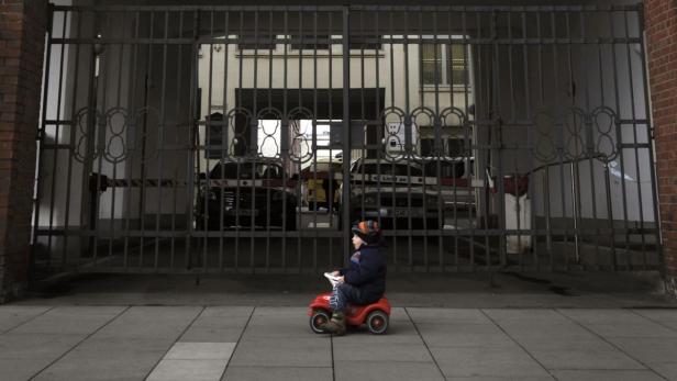 Ein Kind fährt auf einem roten Spielzeugauto vor einem Gittertor.