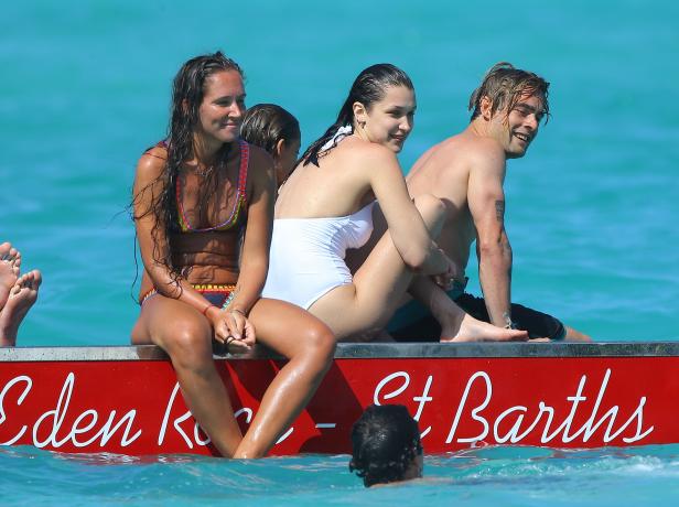 Mehrere Personen sitzen auf einem roten Boot im türkisfarbenen Wasser von St. Barths.