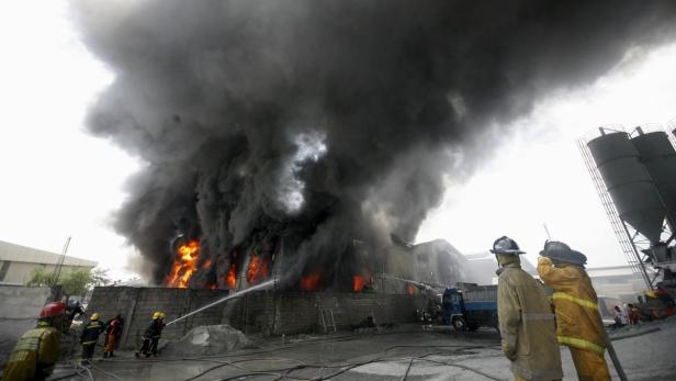 Feuerwehrleute bekämpfen einen Brand in einem Industriegebäude, dichte Rauchwolken steigen auf.