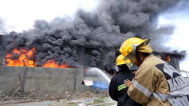Feuerwehrleute bekämpfen einen Brand in einem Gebäude, aus dem dichter Rauch aufsteigt.