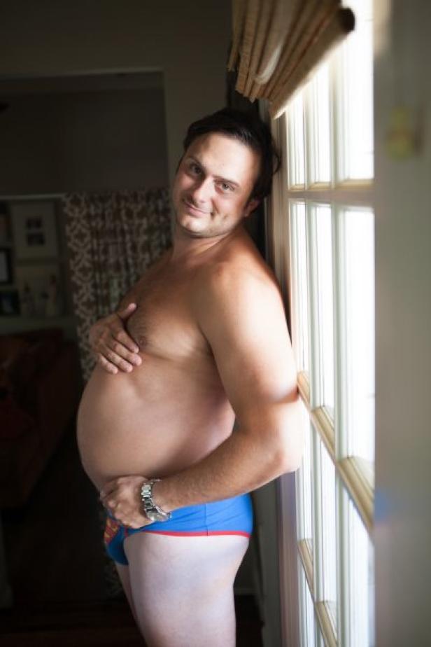 Ein Mann in Superhelden-Unterwäsche posiert mit einem Lächeln am Fenster.