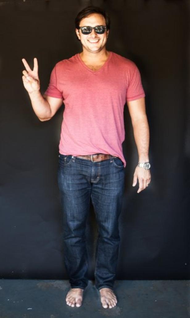 Ein barfüßiger Mann mit Sonnenbrille und T-Shirt zeigt das Friedenszeichen.