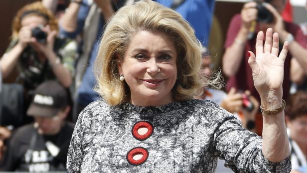 Catherine Deneuve lächelt und winkt in die Menge.