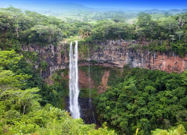 Ein Wasserfall stürzt von einer Klippe, umgeben von üppigem Grün.