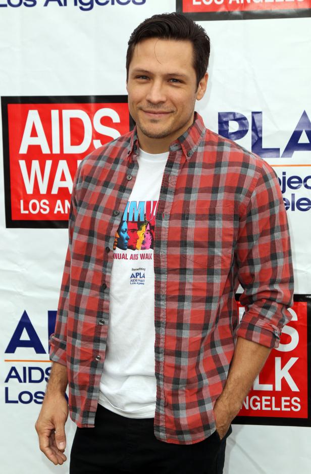 Ein Mann in einem rot-grau karierten Hemd vor einem „AIDS Walk Los Angeles“-Banner.