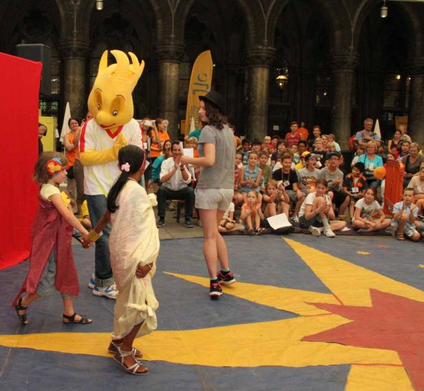Eine Frau moderiert eine Veranstaltung für Kinder mit einem Maskottchen.