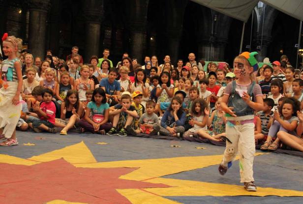 Eine Gruppe Kinder sitzt auf dem Boden und schaut einer Aufführung zu.