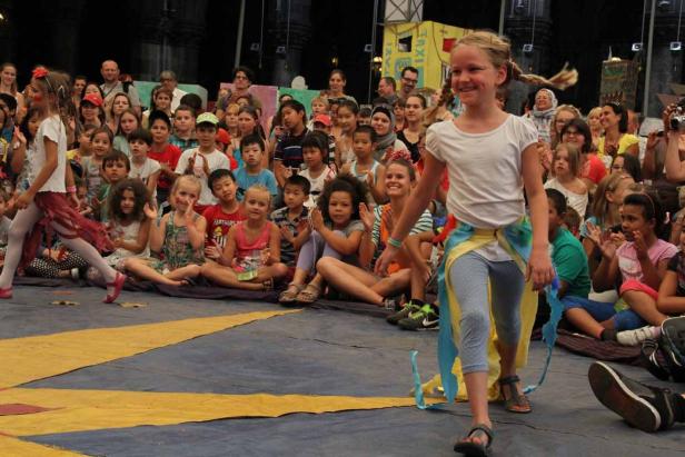 Ein Mädchen läuft vor einer Gruppe von Kindern auf einer Bühne.