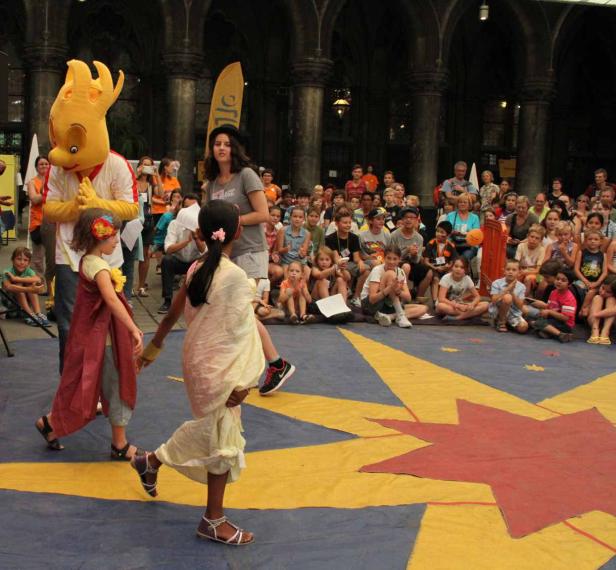 Zwei Mädchen tanzen vor einem Publikum und einem Maskottchen auf einer Bühne.