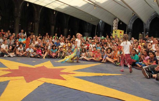 Kinder führen eine Performance vor einem Publikum auf einer Bühne mit Sternenmuster auf.